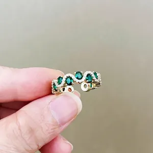 Luxurious gold wavy ring set with five oval green gemstones and small white zircons