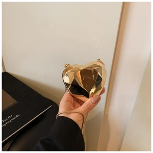 Detail of a mini gold heart-shaped metallic evening clutch with chain strap