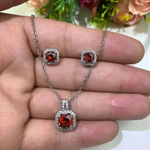 Macro view of silver necklace and stud earrings set with red square-cut zircon stones