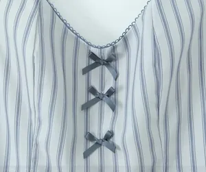 Detail of white striped dress featuring V-neck lace trim and three grey satin bows