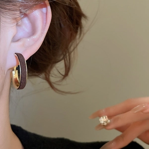 Close-up of C-shaped hoop earrings with dark flocking texture and gold metal lining