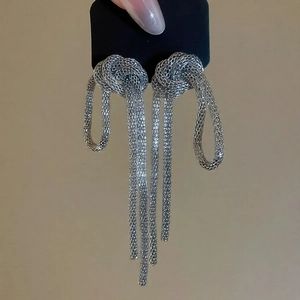 Macro shot of silver woven mesh knot earrings with long tassels on a display card