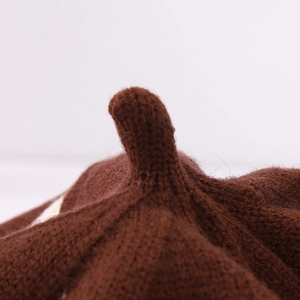 Detailed close-up of dark brown knitted wool texture and top knot on children's beret