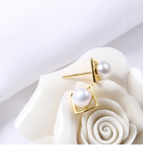 Macro detail of square gold frame pearl earrings resting on a white ceramic flower