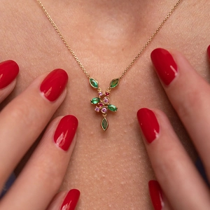Macro shot of hummingbird pendant with green and pink gemstones on gold necklace