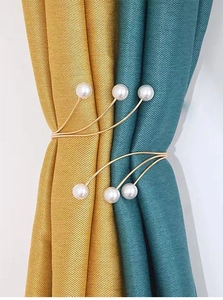 Detail of white pearl curtain tiebacks with elastic gold metal frames on drapes