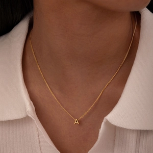Detail of minimalist gold-plated letter A pendant on a fine link chain worn by a model