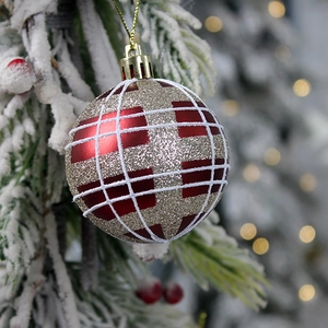 Red and gold plaid Christmas ornament with glitter finish on a snowy pine branch