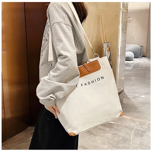Detail of white canvas tote bag featuring brown leather accents and adjustable strap