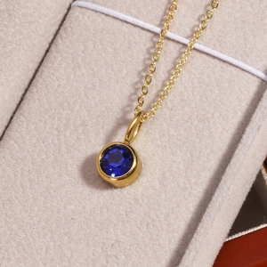 Detailed macro view of a gold birthstone necklace with a blue round gemstone pendant
