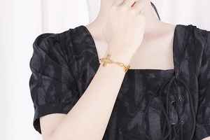 Close-up of a gold cross pendant bracelet with cubic zirconia and OT toggle clasp on wrist