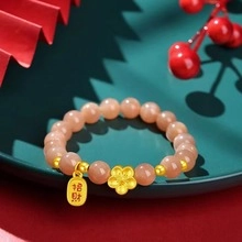 Close-up of sunstone beaded bracelet with gold plum blossom charm and lucky coin tag