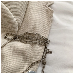 Detail of beige corduroy fabric texture and shiny silver metal chain strap on a kid bag