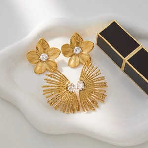 Detailed close-up of gold flower and sunburst earrings with zircons on a white plate