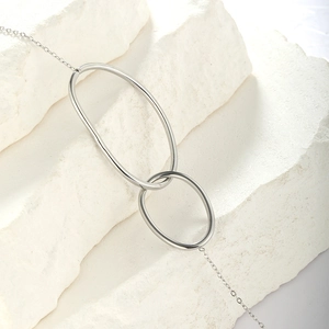 Macro shot of minimalist silver double interlocking oval rings on a white stone background