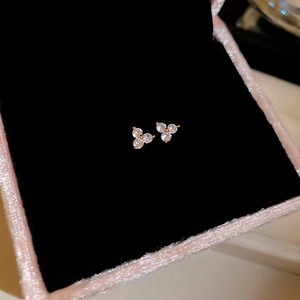 Close-up of gold clover stud earrings with sparkling clear zircons in a black velvet box