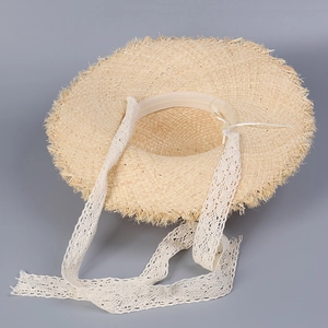 Close-up of handmade straw sun hat featuring white lace ribbons and fringed edges