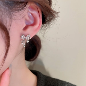 Detail of silver bow tassel earrings with sparkling rhinestones worn on a model ear