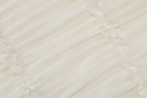 Dettaglio del tessuto plissettato bianco crema con bordo in pizzo e trama morbida