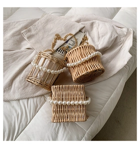 Three assorted woven straw bags with pearl handles and gold chain straps on white bedding