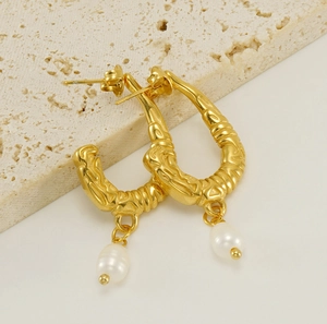 Macro detail of U-shaped gold earrings with textured metal finish and white pearls