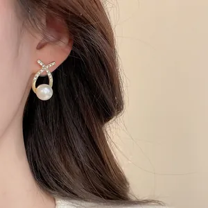 Gros plan d'une boucle d'oreille en perle avec structure dorée et zircons sur modèle
