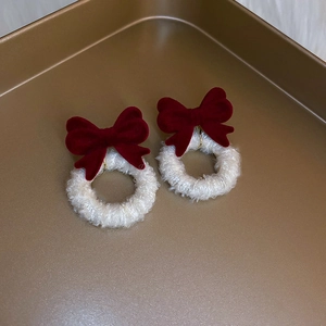 Close-up of red velvet bow earrings with white faux fur rings on a gold jewelry tray