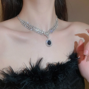Detailed close-up of oval blue zircon pendant necklace on a model with black feather top