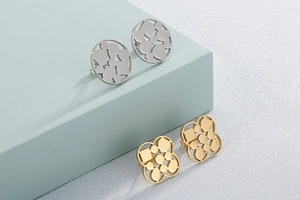 Detail of silver geometric circular and gold floral hollow earrings on blue stands