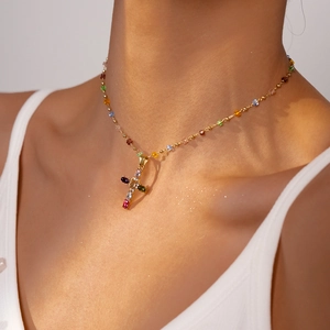 Close-up of a gold-plated cross necklace with colorful gemstones on a female collarbone