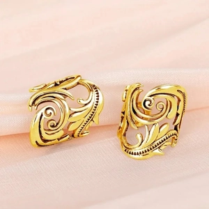 Macro detail of vintage gold leaf ear cuffs with intricate hollow swirl baroque patterns