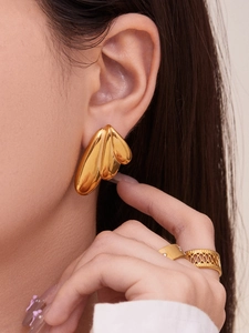 Detailed close-up of 18k gold-plated angel wing earrings and geometric open ring on a model