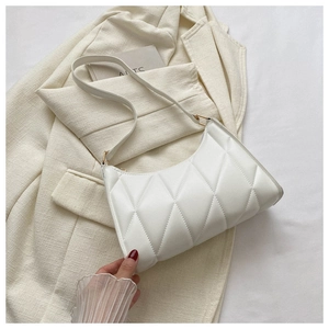 Detailed view of white quilted faux leather baguette bag on a beige blazer background