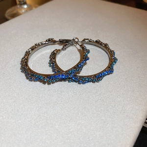 Macro shot of silver twisted hoop earrings featuring paved blue crystals and silver finish