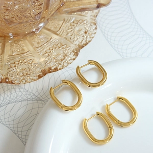 Polished 18K gold-plated U-shaped geometric earrings on a minimalist white ceramic surface