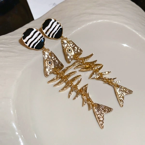 Macro view of gold fishbone earrings with black and white stripes on a ceramic plate