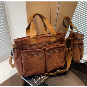 Detail of brown corduroy tote bag featuring multiple front zip pockets and beige handles