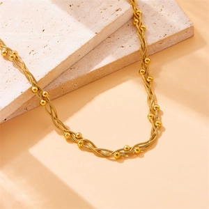Gold plated stainless steel chain necklace with beads on minimalist stone background