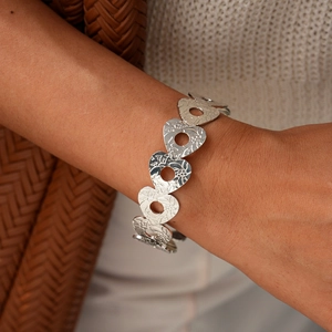Dettaglio di un bracciale argento con maglie a cuore traforate e trame incise sul polso