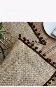 Detail of woven jute table runner featuring rustic brown pom-pom fringe on a wooden table