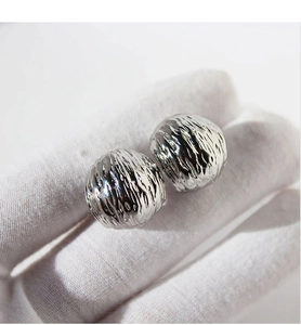 Macro shot of silver ball stud earrings with unique lava texture on a white gloved hand