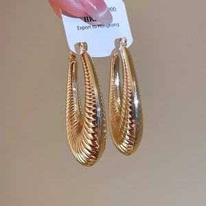 Detailed close-up of large golden C-shaped hoop earrings with spiral ribbed texture