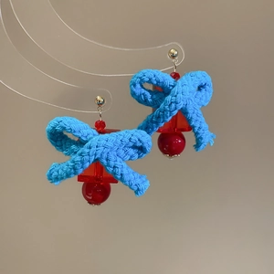 Detailed shot of blue woven bow earrings with red resin pendants and gold studs
