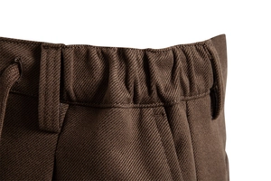 Detail of brown trousers featuring an elastic waistband with drawstring and twill fabric texture
