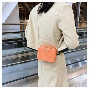 Detail of orange quilted PVC jelly bag with a gold chain strap worn by a model