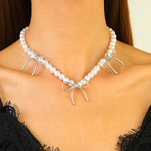 Elegant white pearl necklace featuring silver bow accents worn on a female neck and chest