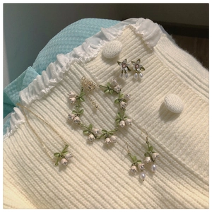 Detail of lily of the valley jewelry set with white flowers and green enamel leaves