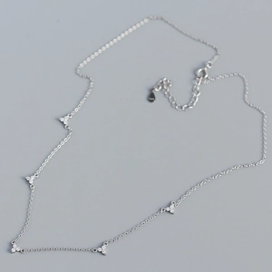 Gros plan d'un collier en argent S925 avec trèfles en zircon sur fond gris neutre