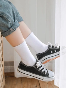 Close-up of white mid-calf cotton socks for children styled with black canvas sneakers