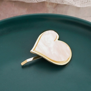 Close-up of golden heart ponytail hair hook with white marble texture on ceramic plate